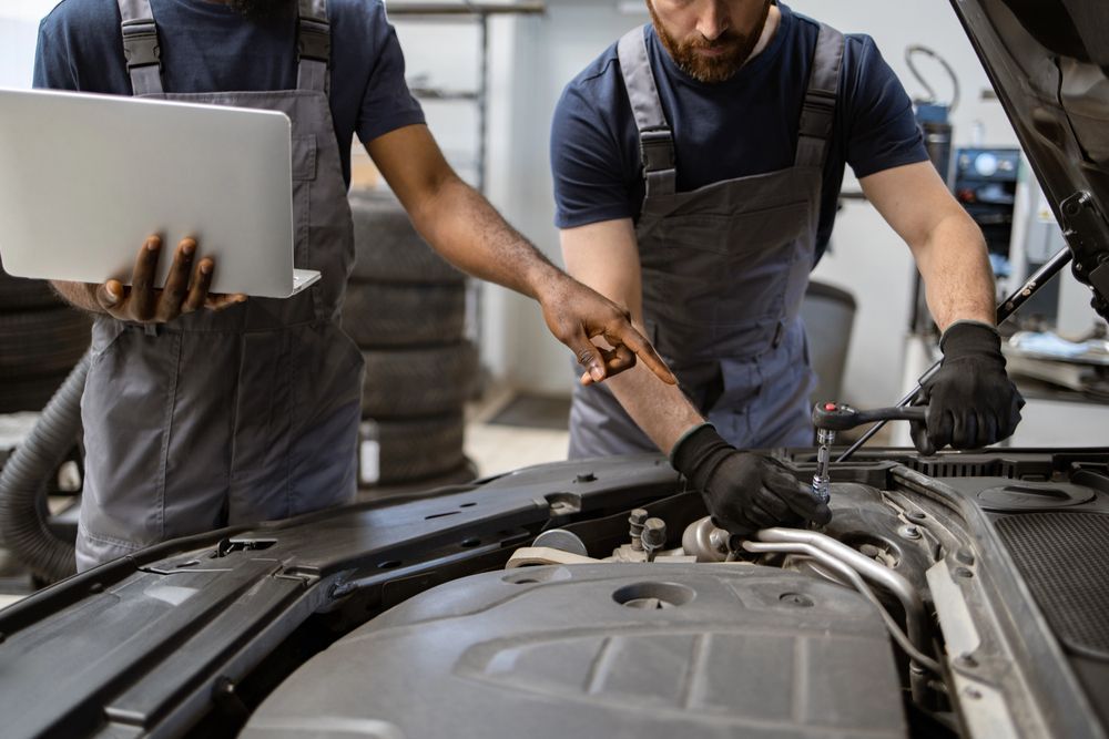 Dos mecánicos trabajando en el motor de un coche con un ordenador portátil, en un taller de reparación.