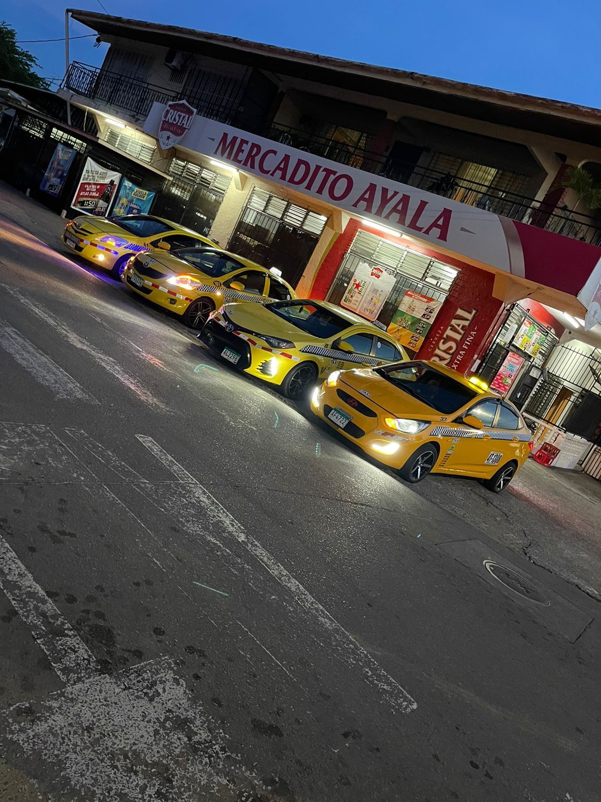 Cinco coches amarillos aparcados en diagonal frente a una tienda con un cartel rojo. Escena callejera.
