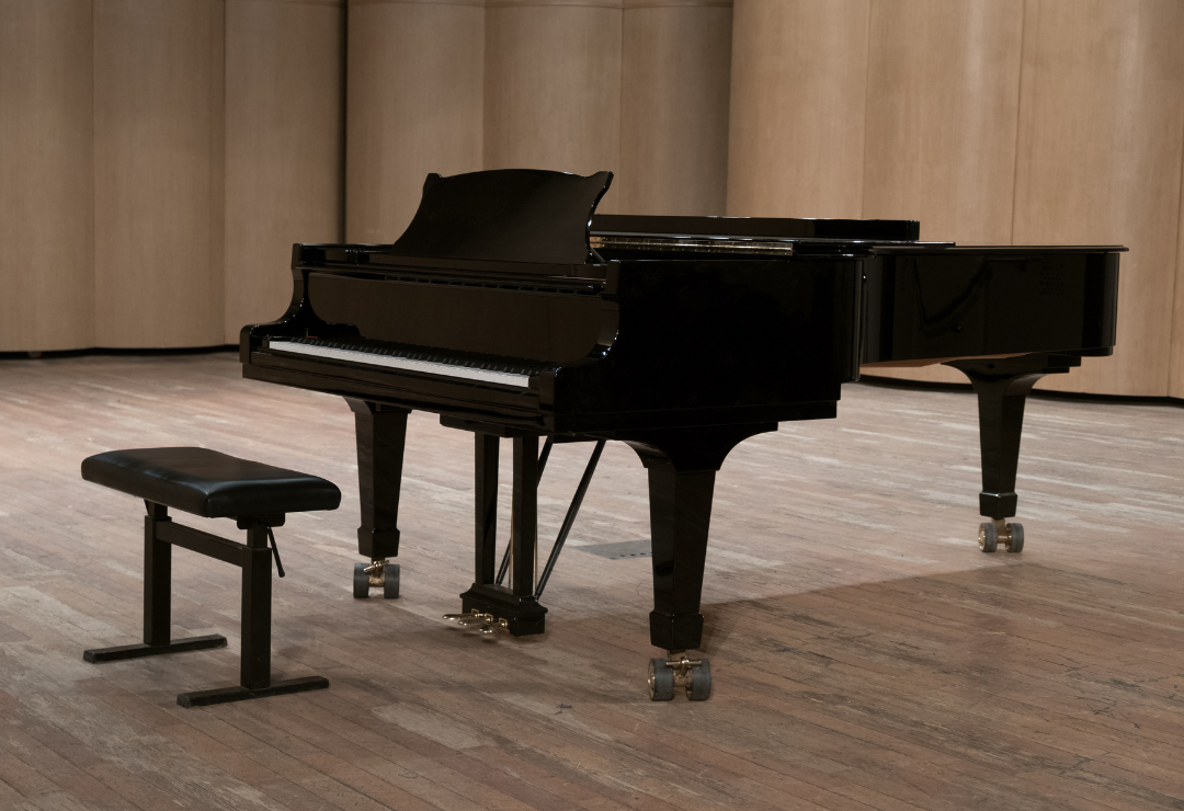 A baby grand piano on a hardwood floor, alone with the seat in front of it