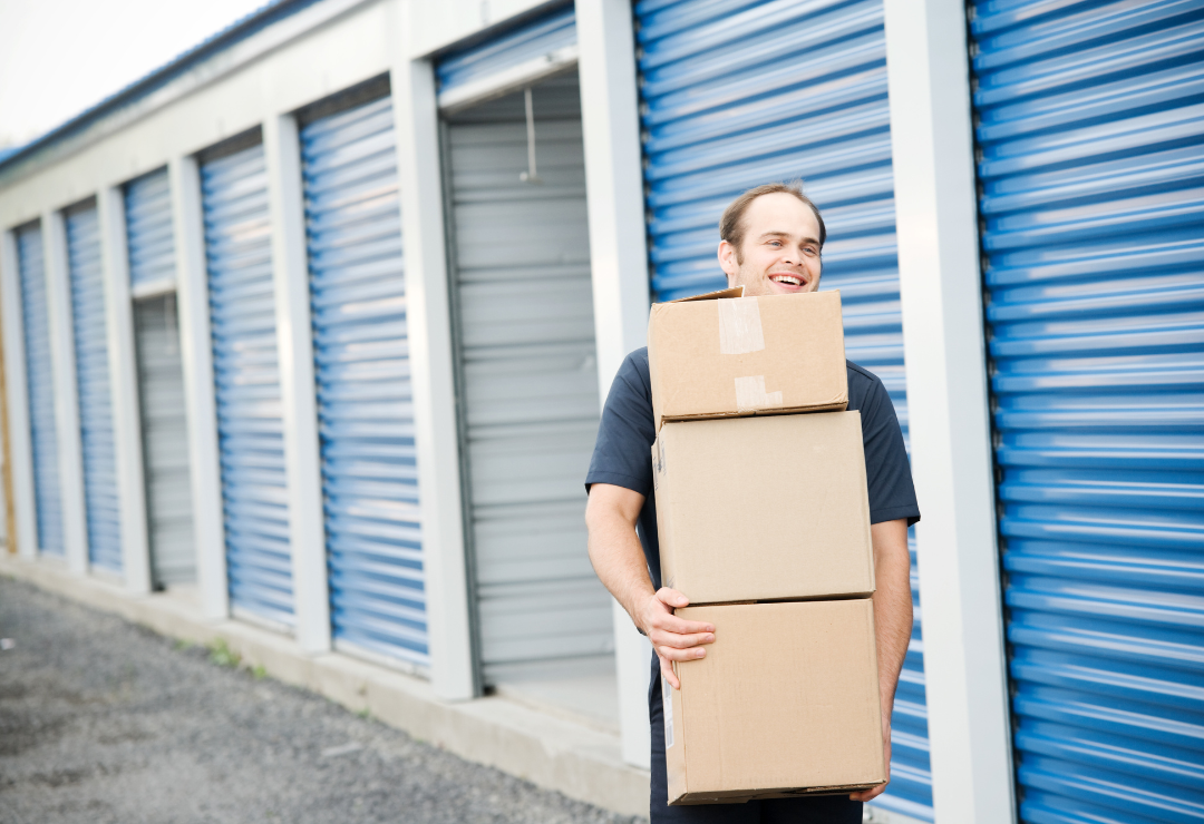 A man in front of storage lockers carrying a stack of cardboard boxes