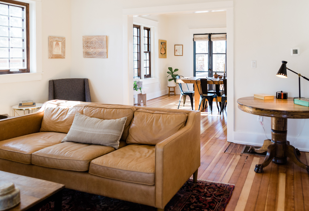 A leather couch in a living room with a hardwood floor and wooden side table