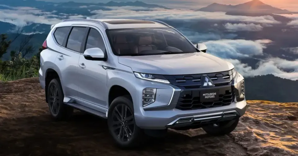 Homem de terno dirigindo um carro, mãos no volante. Interior desfocado, luz forte. Texto: