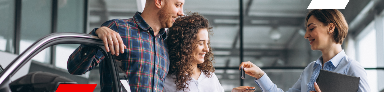 Um casal recebendo as chaves do carro de um vendedor dentro de uma concessionária.