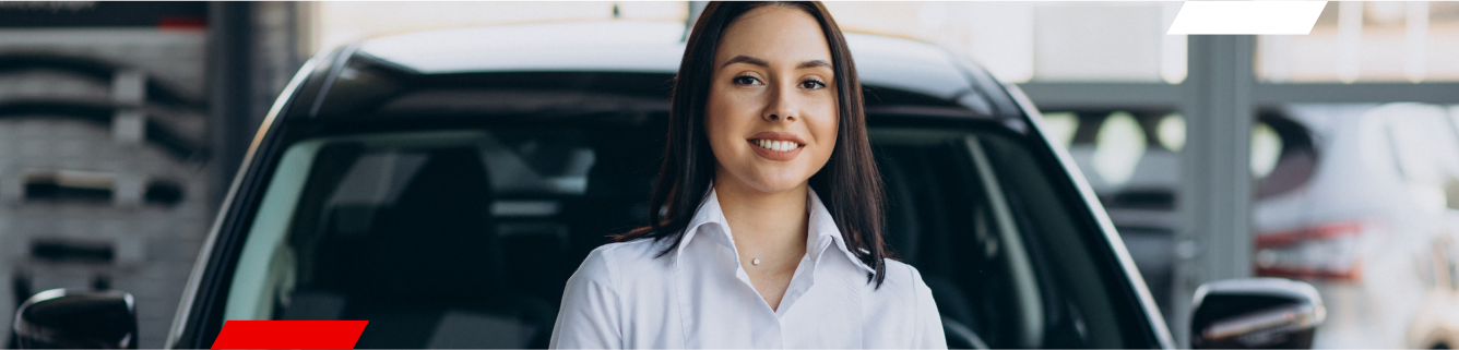Mulher de camisa branca sorrindo em frente a um carro preto em uma concessionária de veículos.