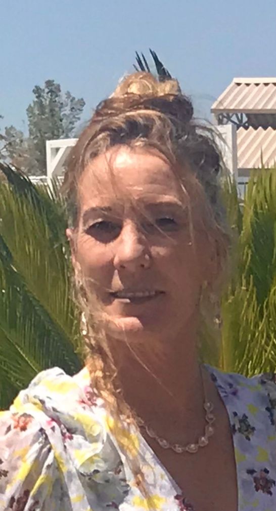A woman with a bun in her hair is standing in front of a palm tree.