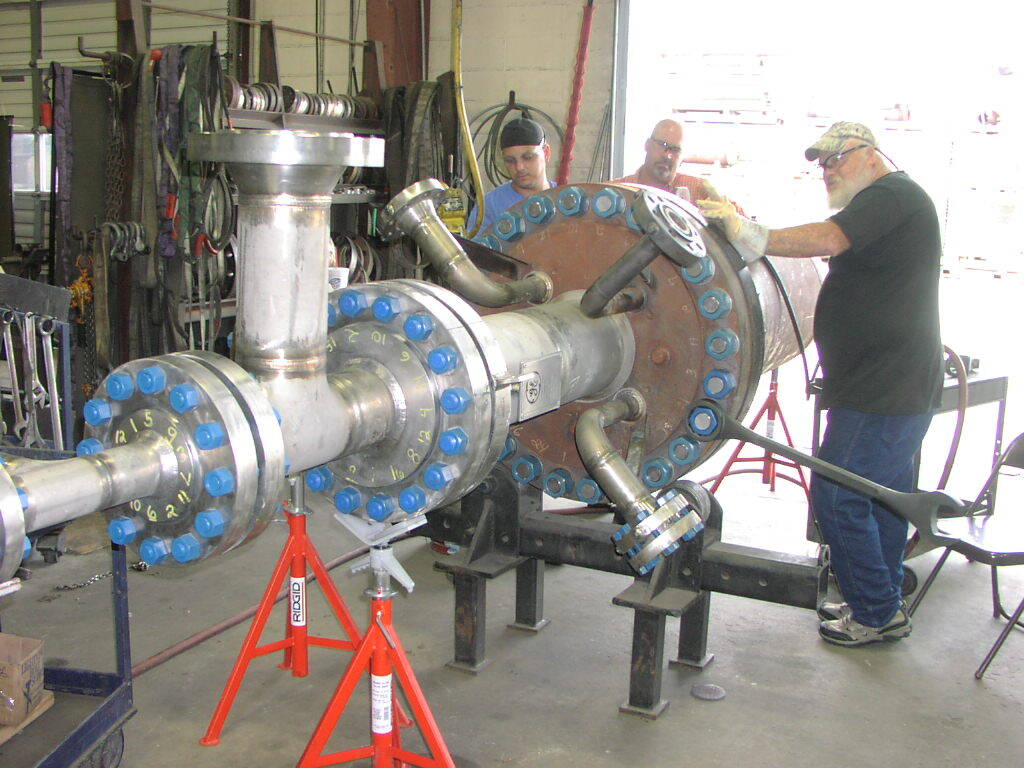 Two men are working on a large metal pipe in a factory.