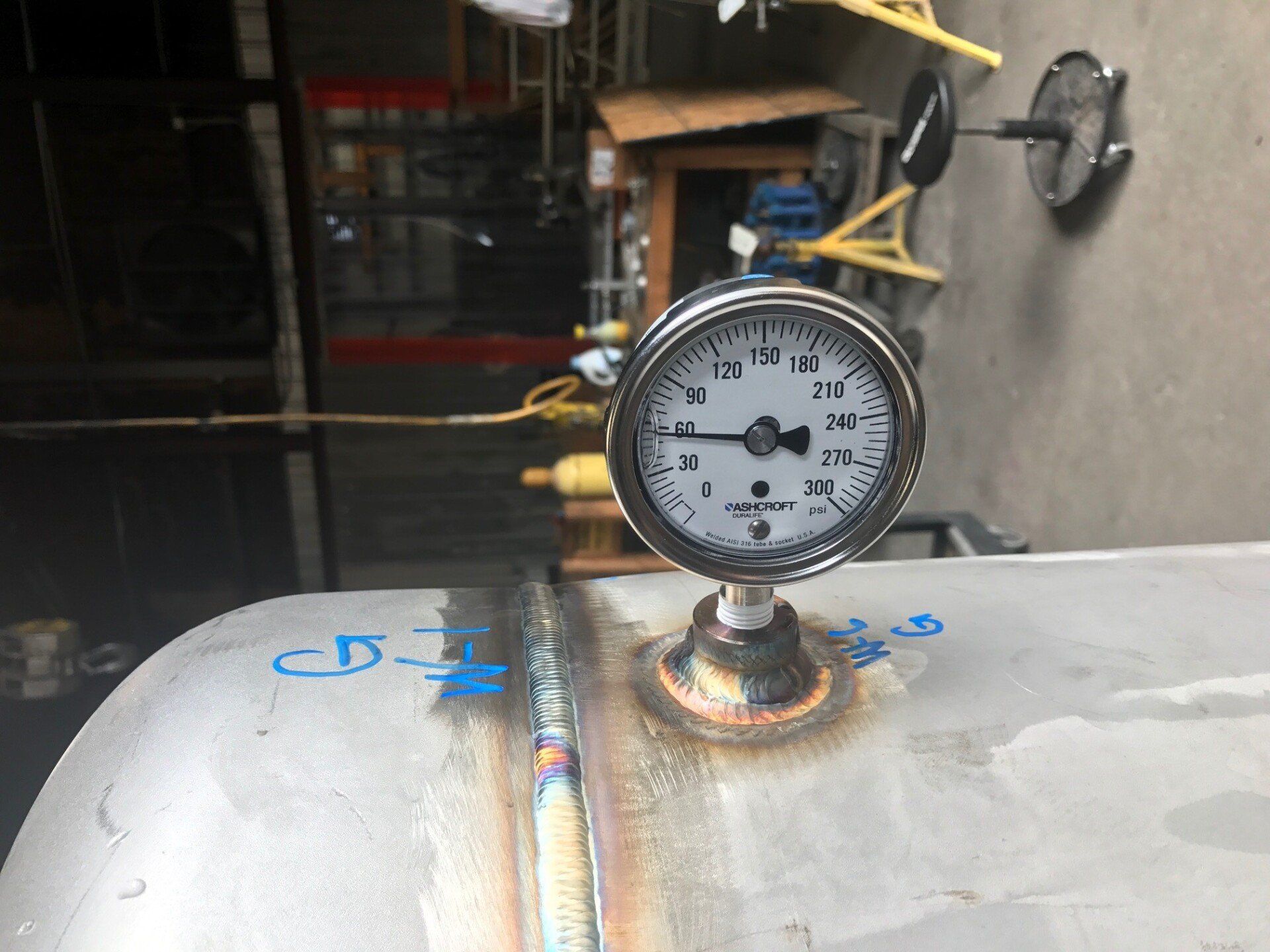 A pressure gauge is sitting on top of a stainless steel tank.