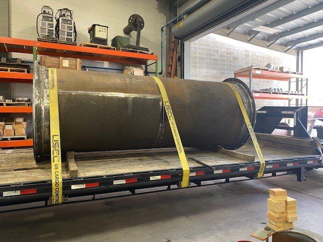 A large metal pipe is sitting on top of a trailer in a warehouse.