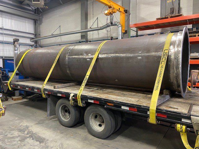 A large metal pipe is sitting on top of a trailer.