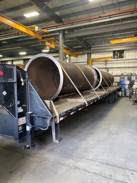 A large pipe is sitting on top of a trailer in a factory.