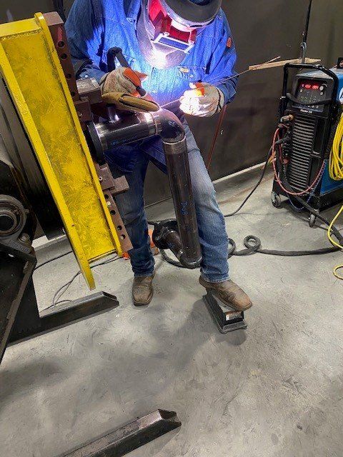 A man wearing a welding mask is welding a pipe in a factory.
