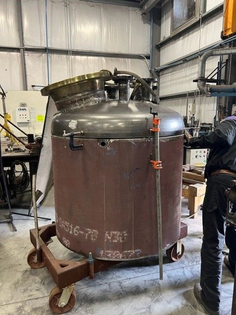 A large metal tank is sitting on a cart in a factory.