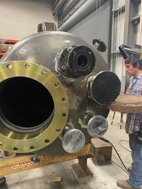 A man is welding a large metal object in a factory.