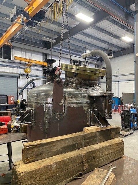 A large machine is being lifted by a crane in a factory