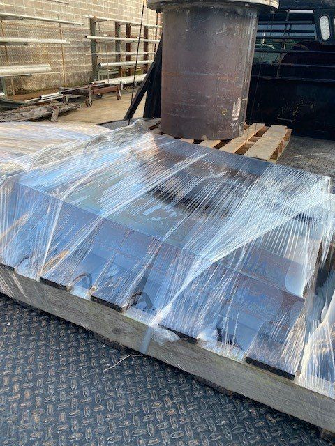 A large piece of metal is wrapped in plastic and sitting on top of a wooden pallet.