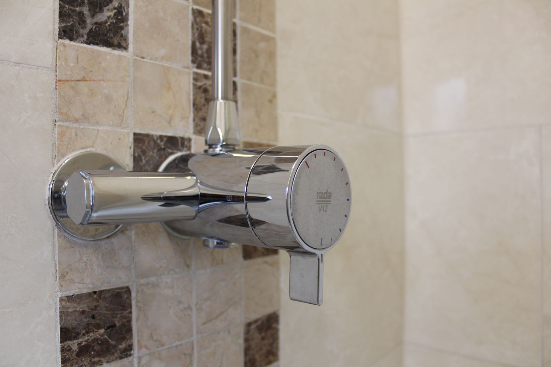 Shiny chrome shower faucet mounted on patterned beige and brown tiles.
