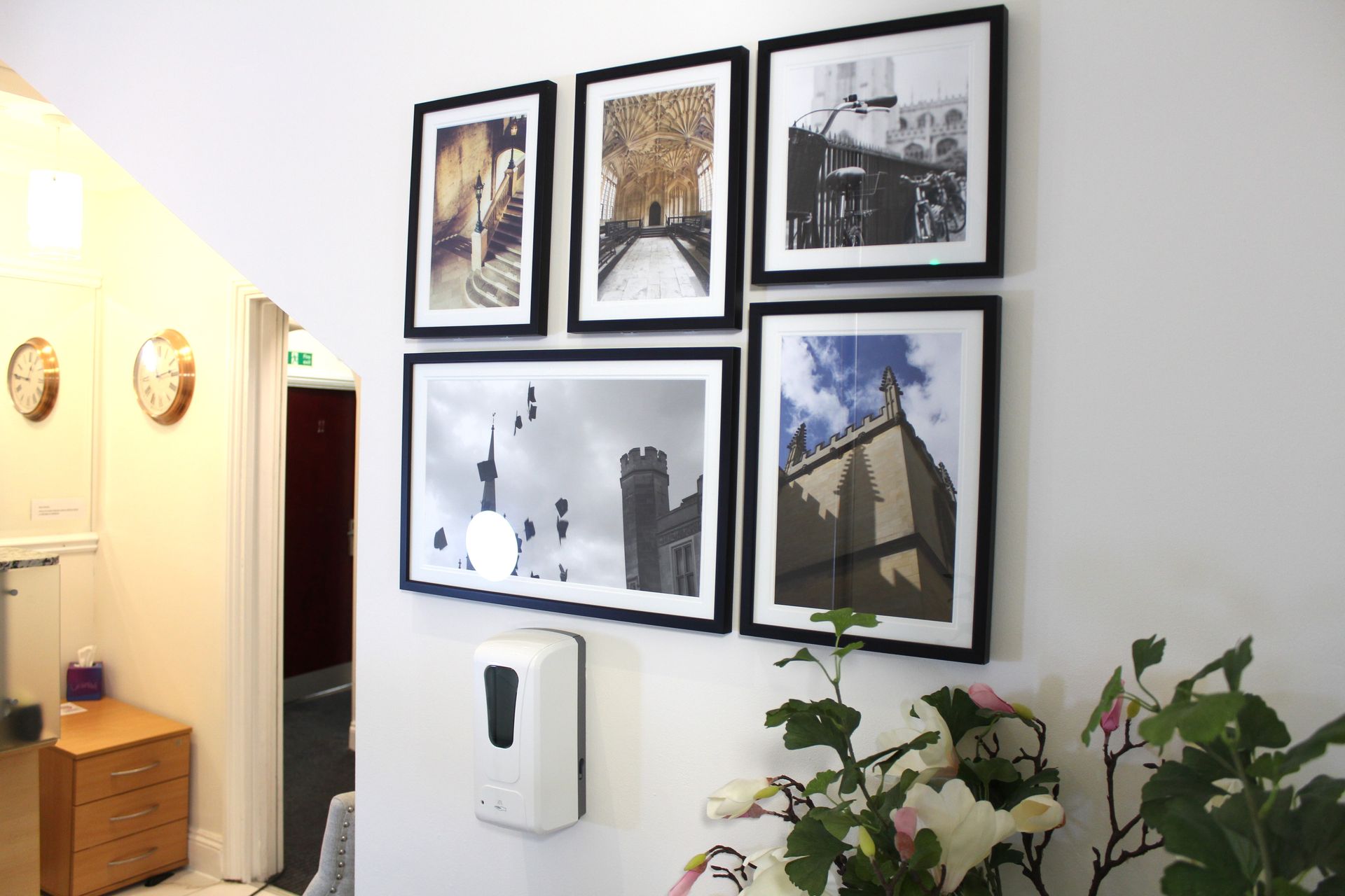 Wall with framed photos, a hand sanitizer dispenser, and decorative plants.