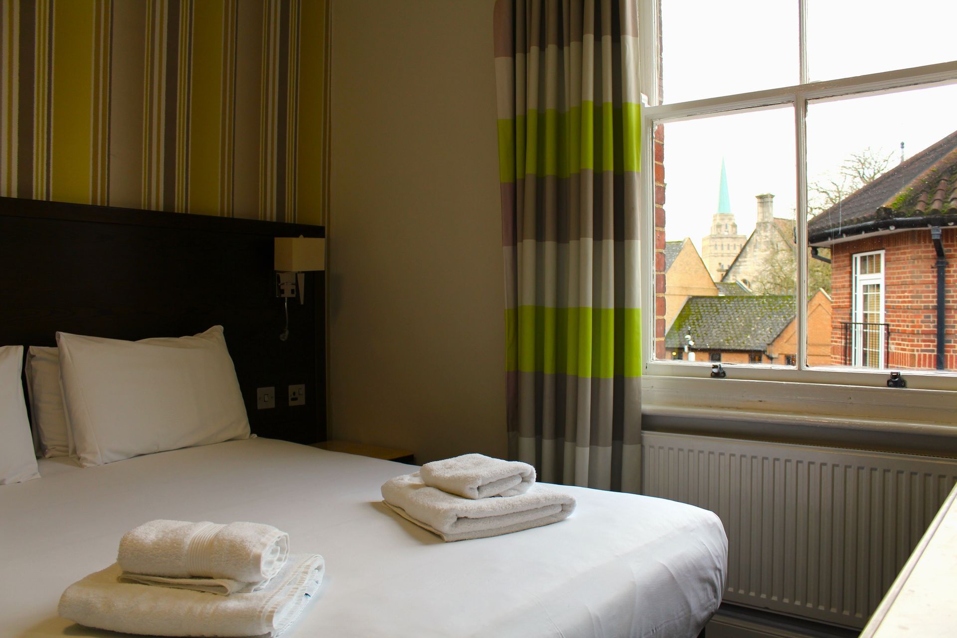 Hotel bedroom with a bed, towels, window, and view of buildings and a steeple.