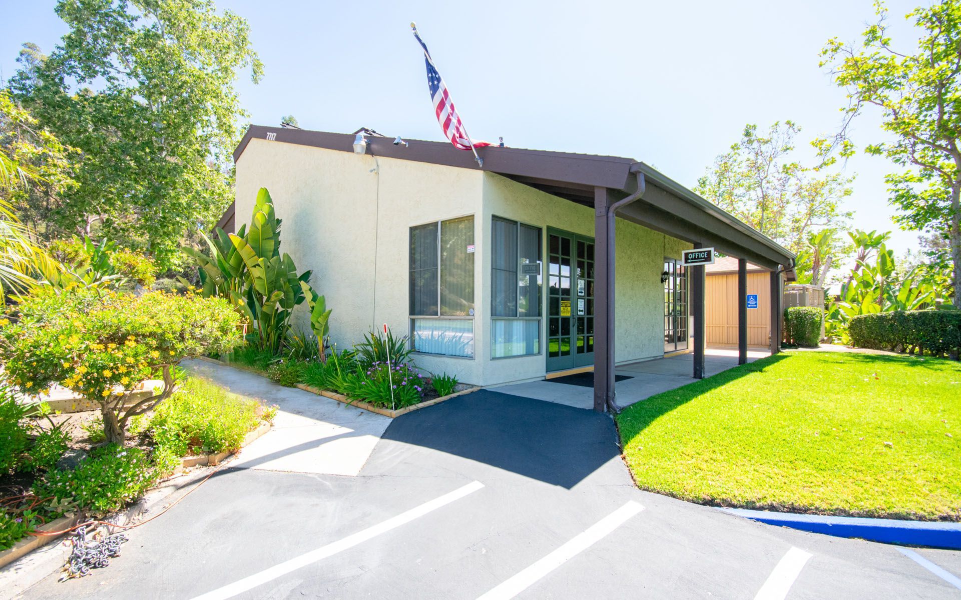 A one-story building with American flag, a brown overhang, and a short walkway at Cowles Landing, offer apartments in San Diego, CA.