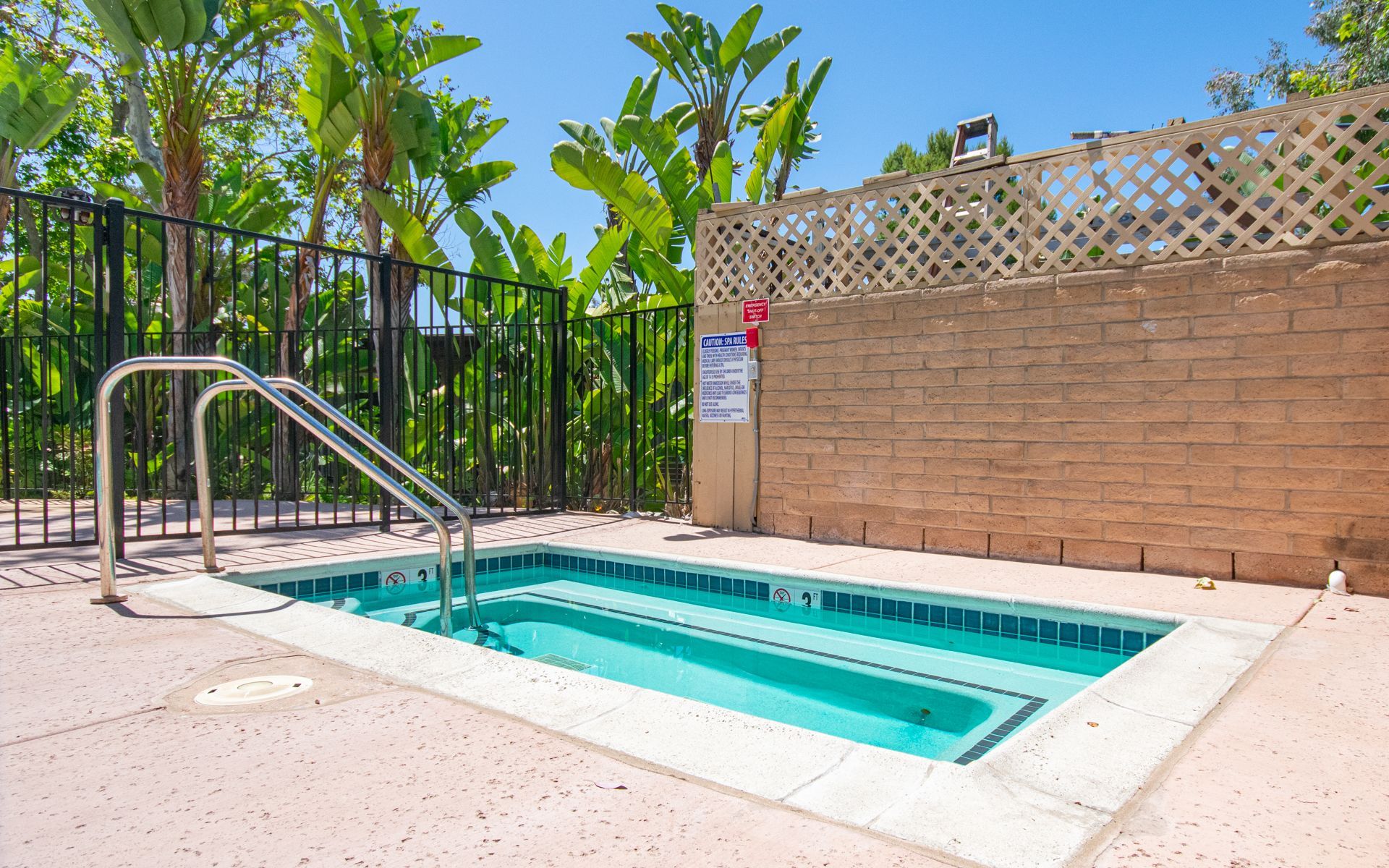 Small turquoise hot tub with stainless steel handrails, next to a brick wall and a fence, outdoors at Cowles Landing, offer apartments in San Diego, CA.