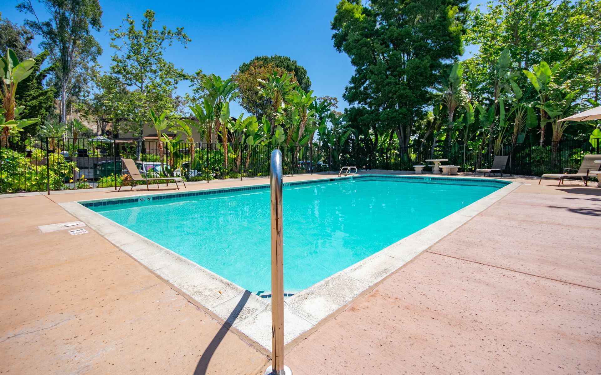 Pool with bright blue water, surrounded by concrete deck and lush green trees at Cowles Landing, offer apartments in San Diego, CA.