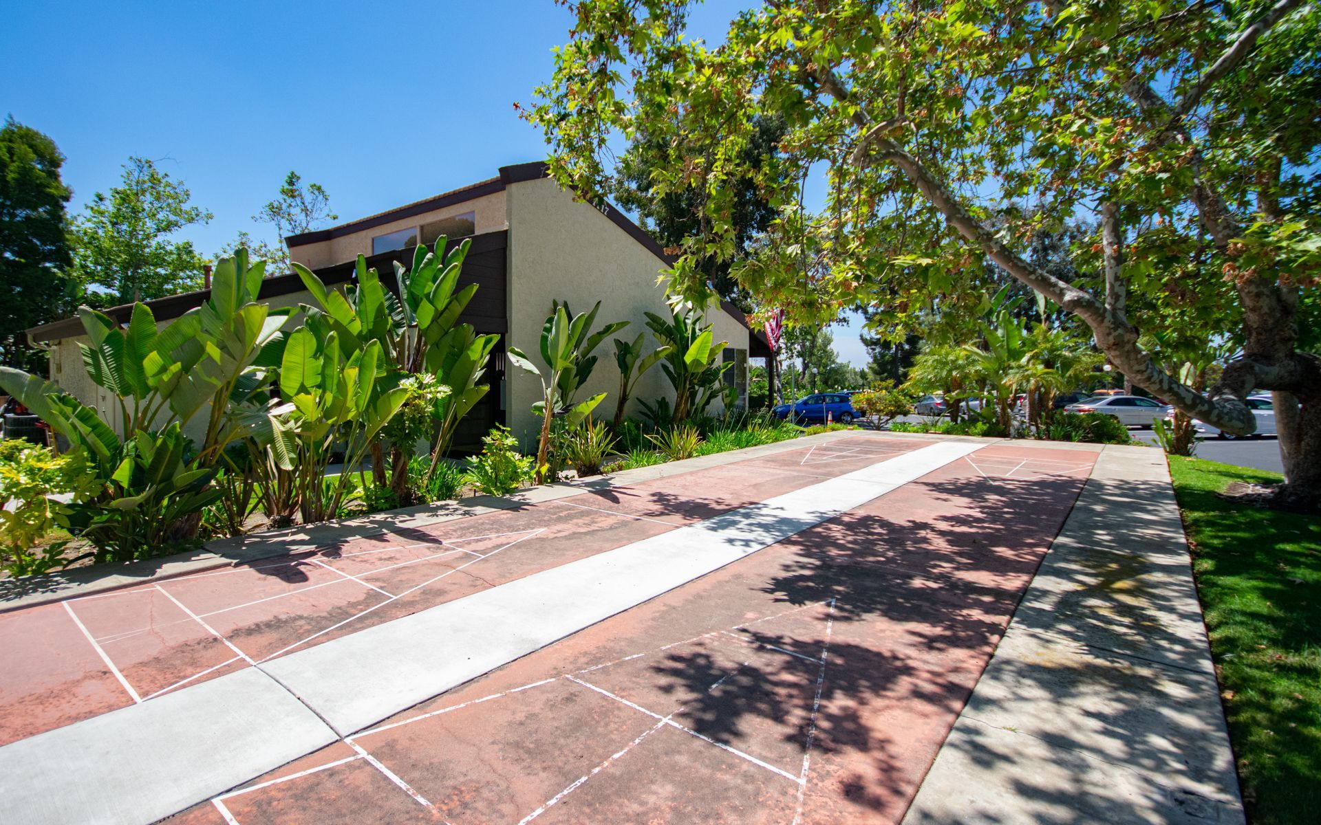 Driveway with red brick paving, flanked by greenery and a building under a bright blue sky.