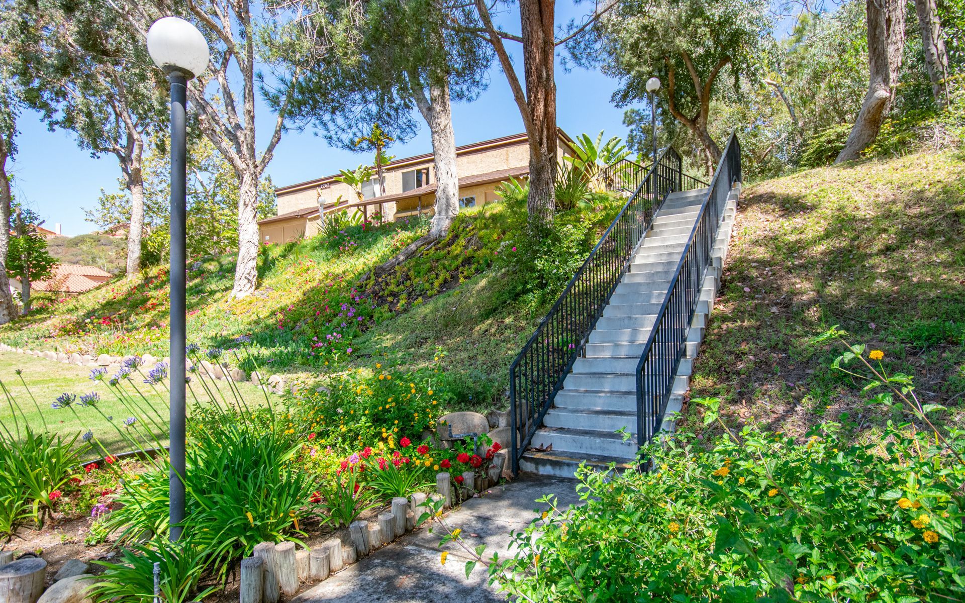 Stone staircase ascends a grassy hillside, leading to a building. Greenery and flowers line the path.