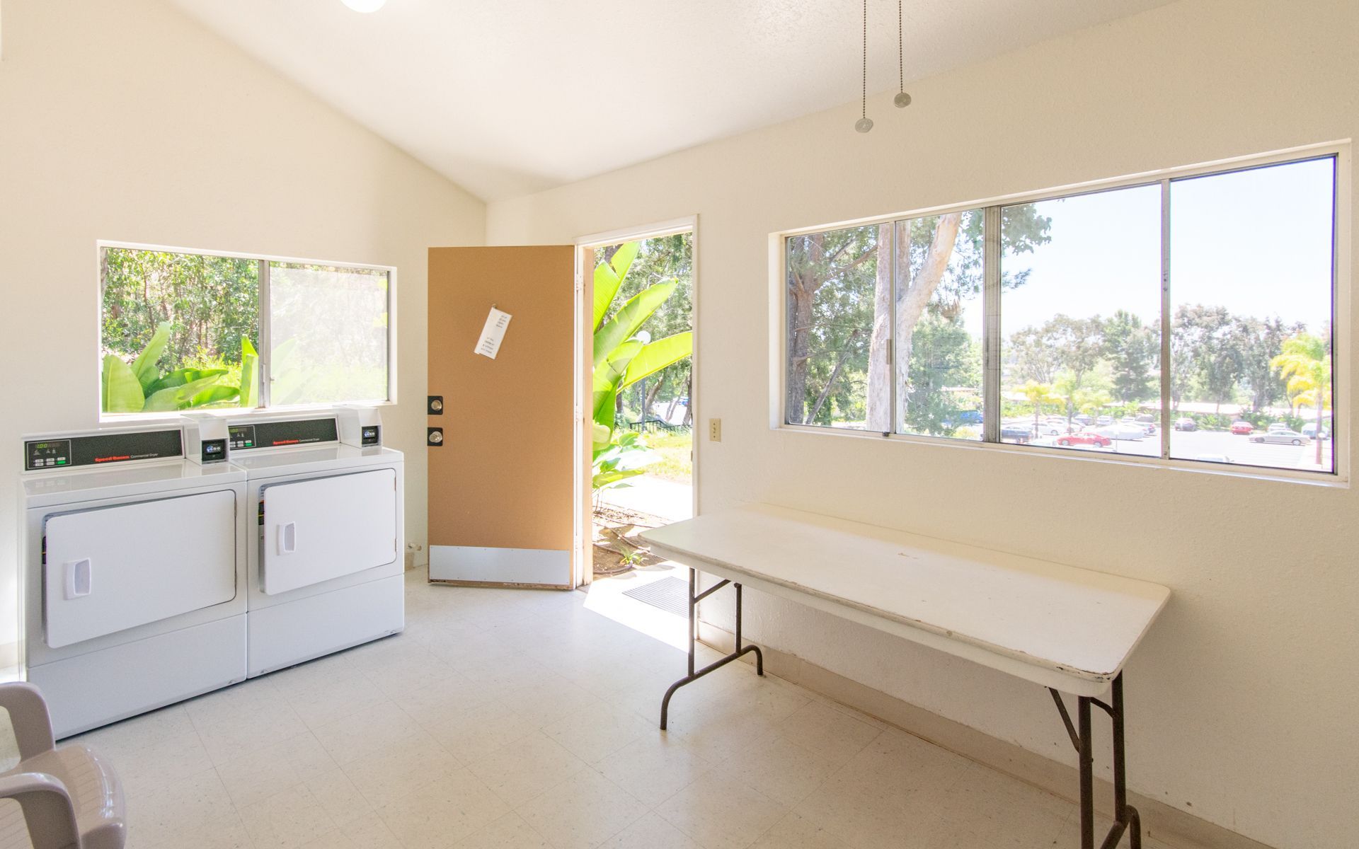 Laundry room with two washers, a folding table, and a door open to the outside at Cowles Landing, offering apartments in San Diego, CA.