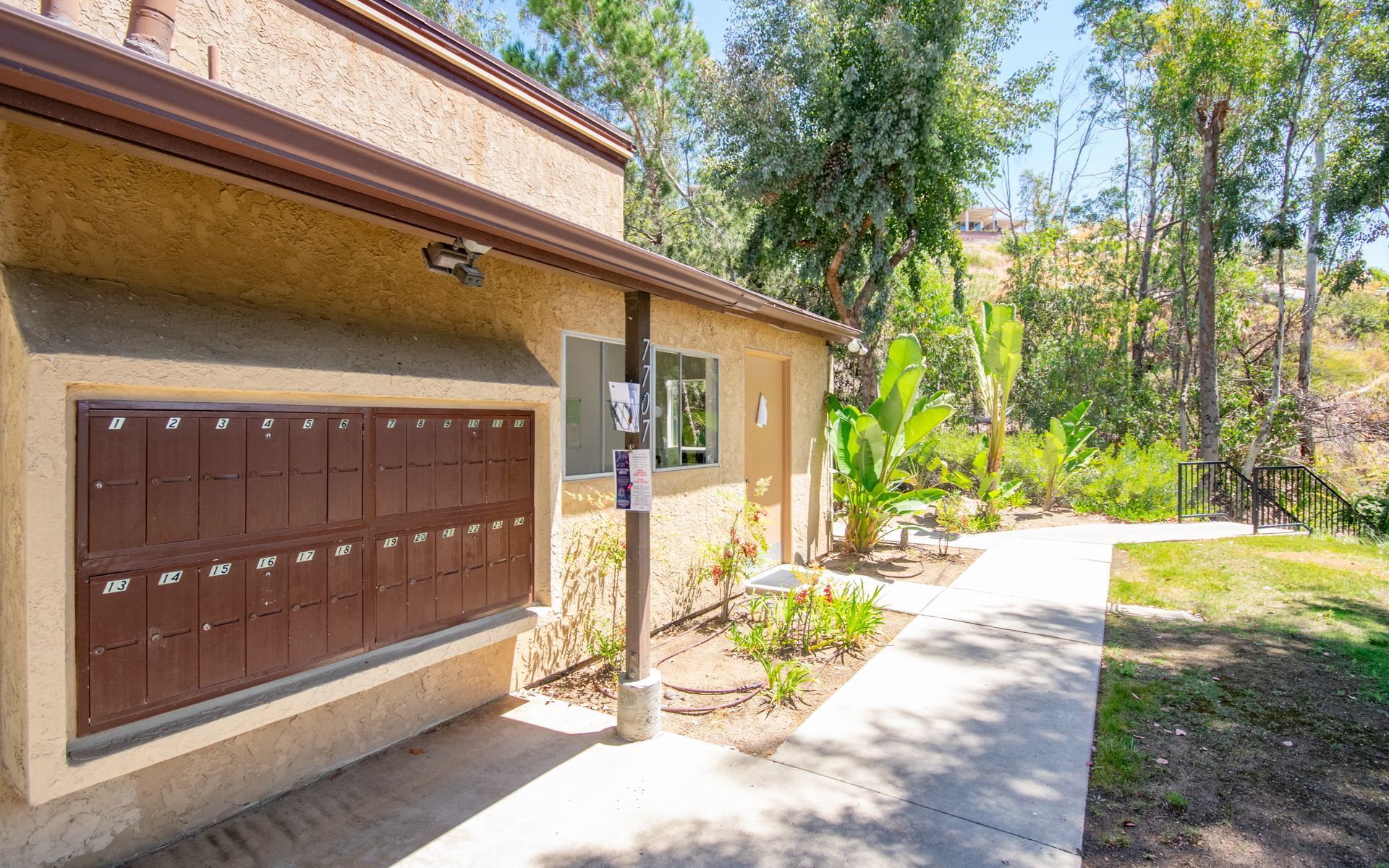 Tan building with brown mailboxes, walkway, and greenery at Cowles Landing, offer apartments for rent in San Diego, CA.