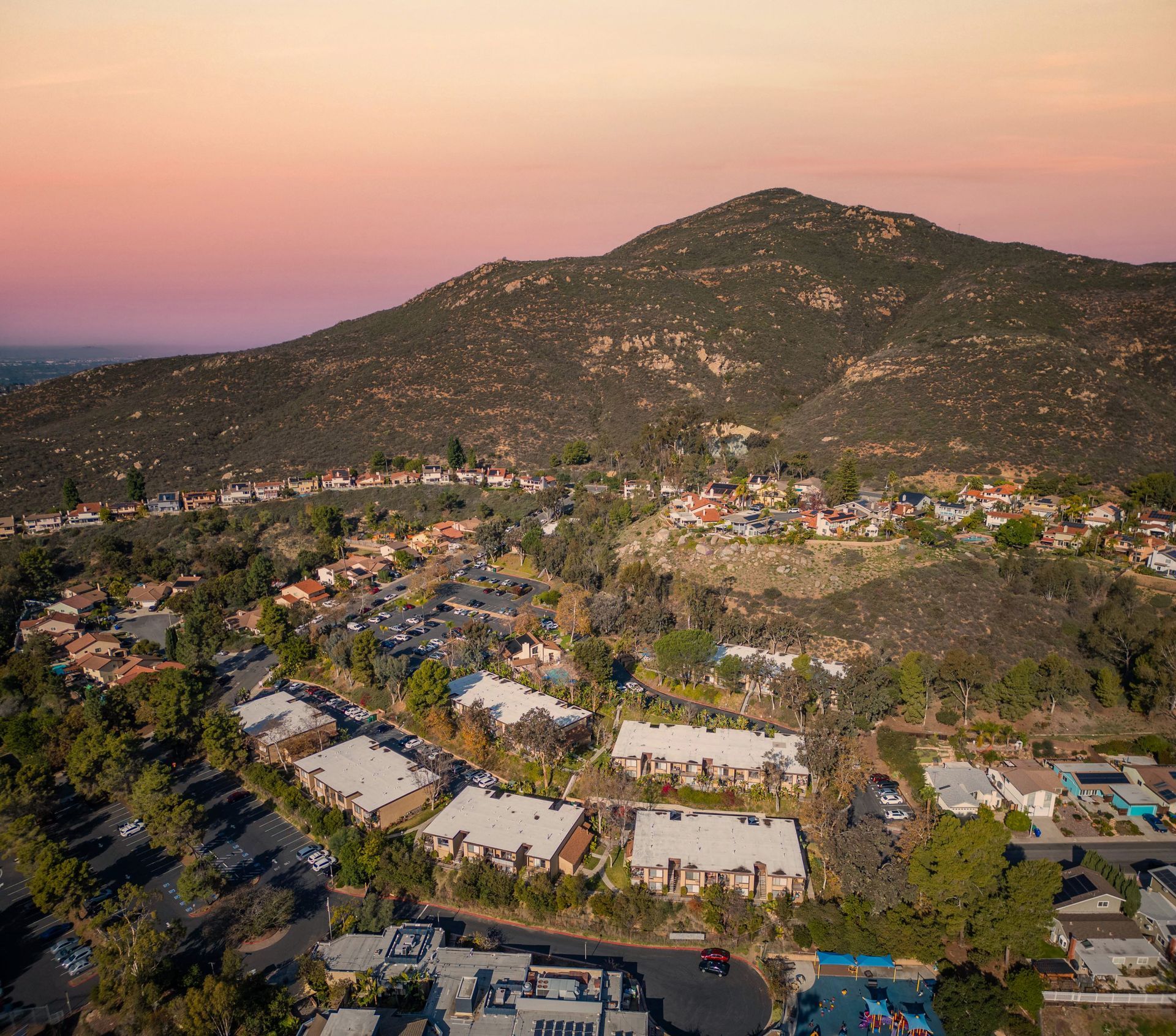 Aerial view of a suburban neighborhood and mountain at sunset; golden sky.