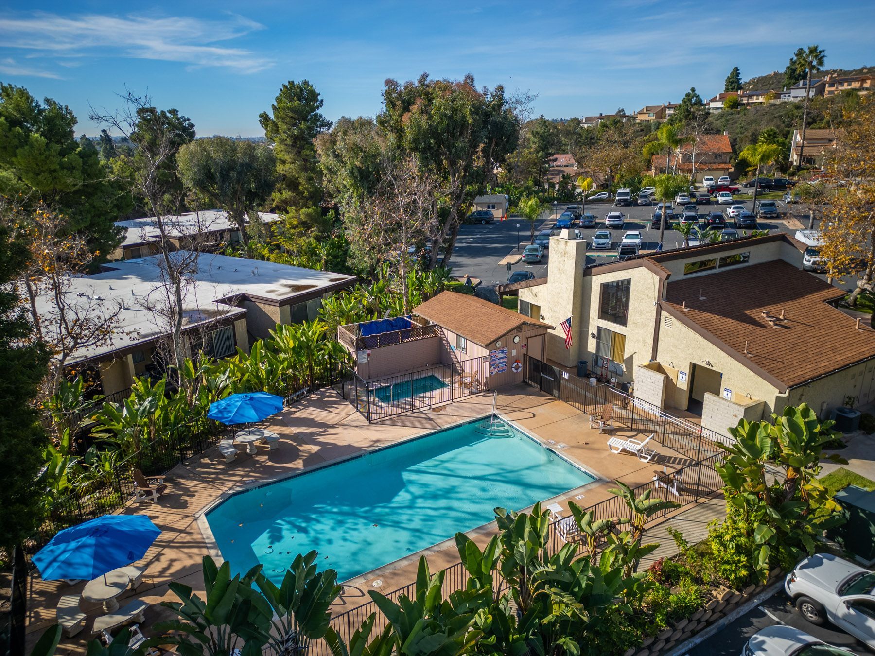 Aerial view of an apartment complex with a pool, trees, and parked cars under a blue sky at Cowles Landing in San Diego, CA.