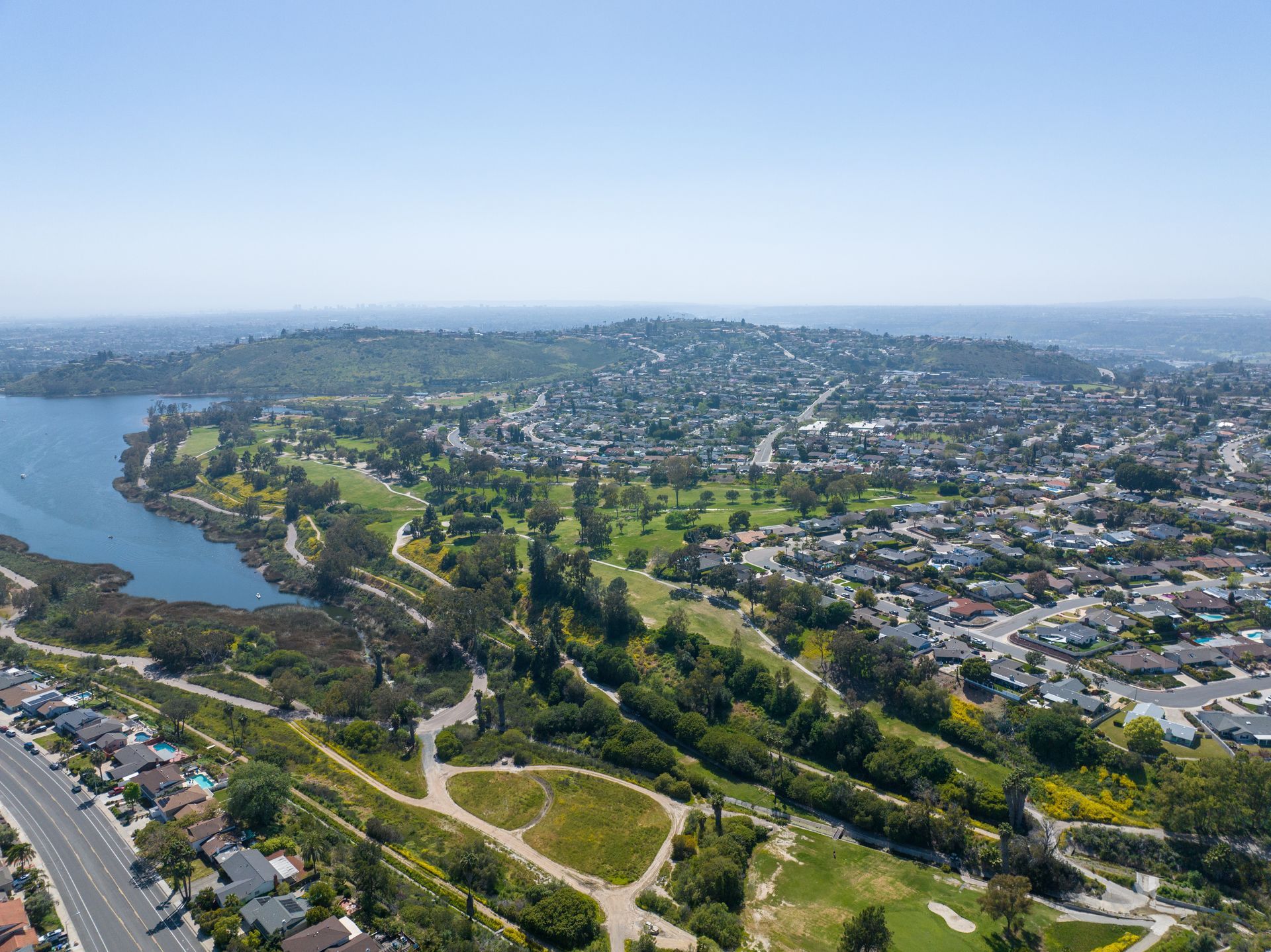 Aerial view of a city with a lake, golf course, and residential neighborhoods under a clear blue sky at Cowles Landing in San Diego, CA.