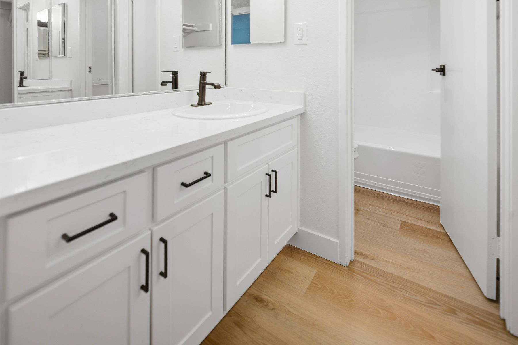 White bathroom with vanity and black hardware, open door leads to shower.