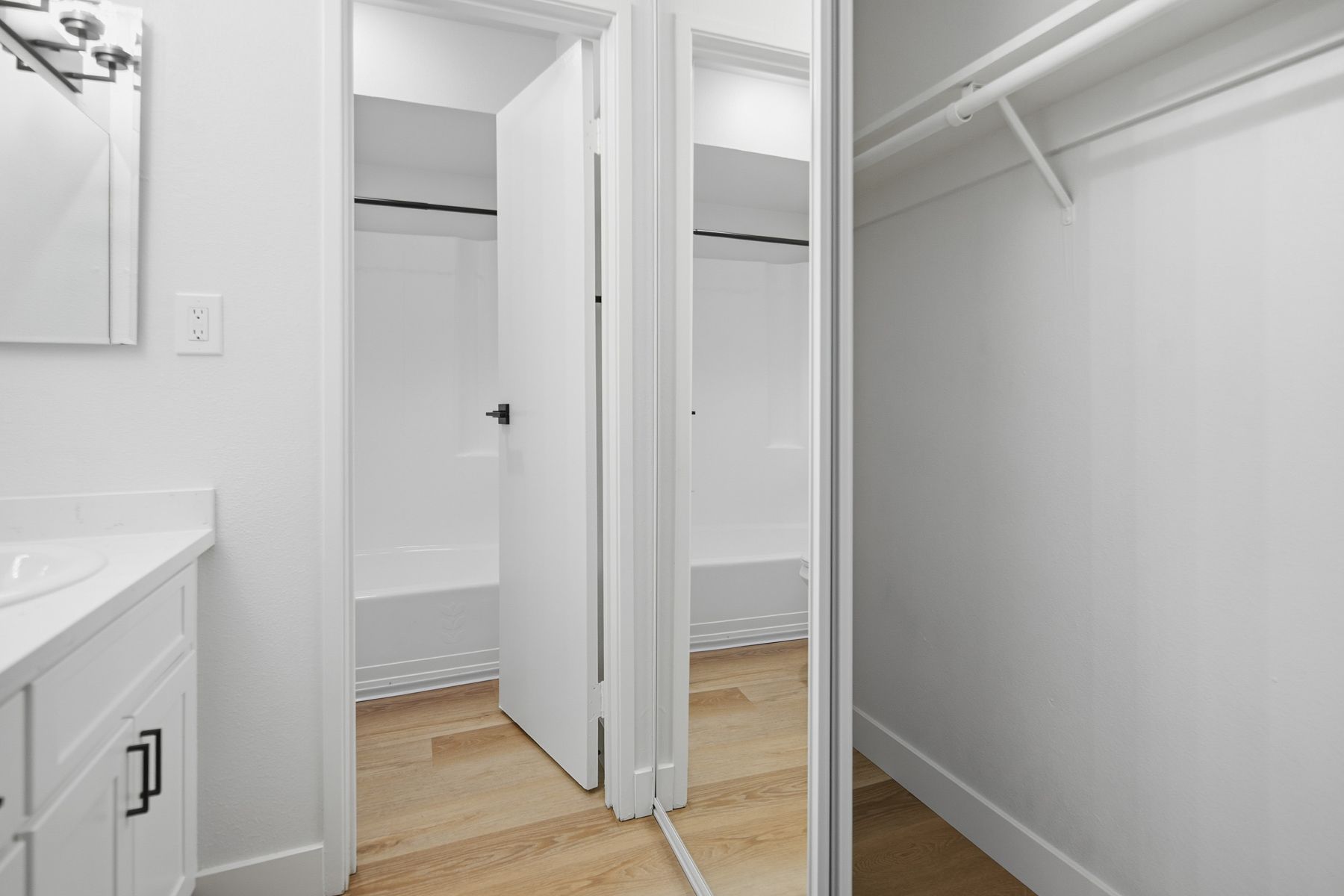 White bathroom with open door revealing a shower. A mirrored closet is on the right.