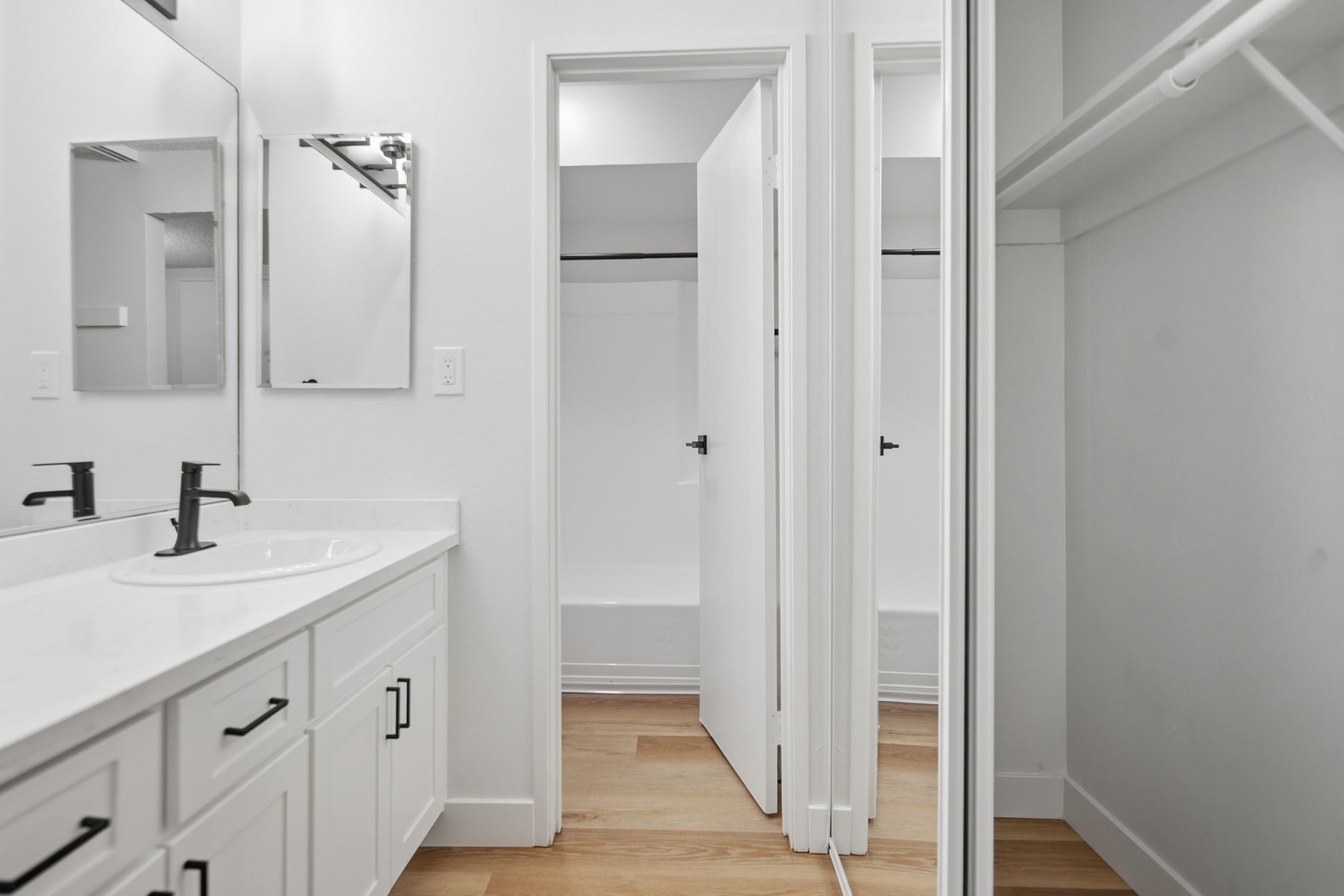 White bathroom with sink, mirror, and open doorway leading to a shower and closet.