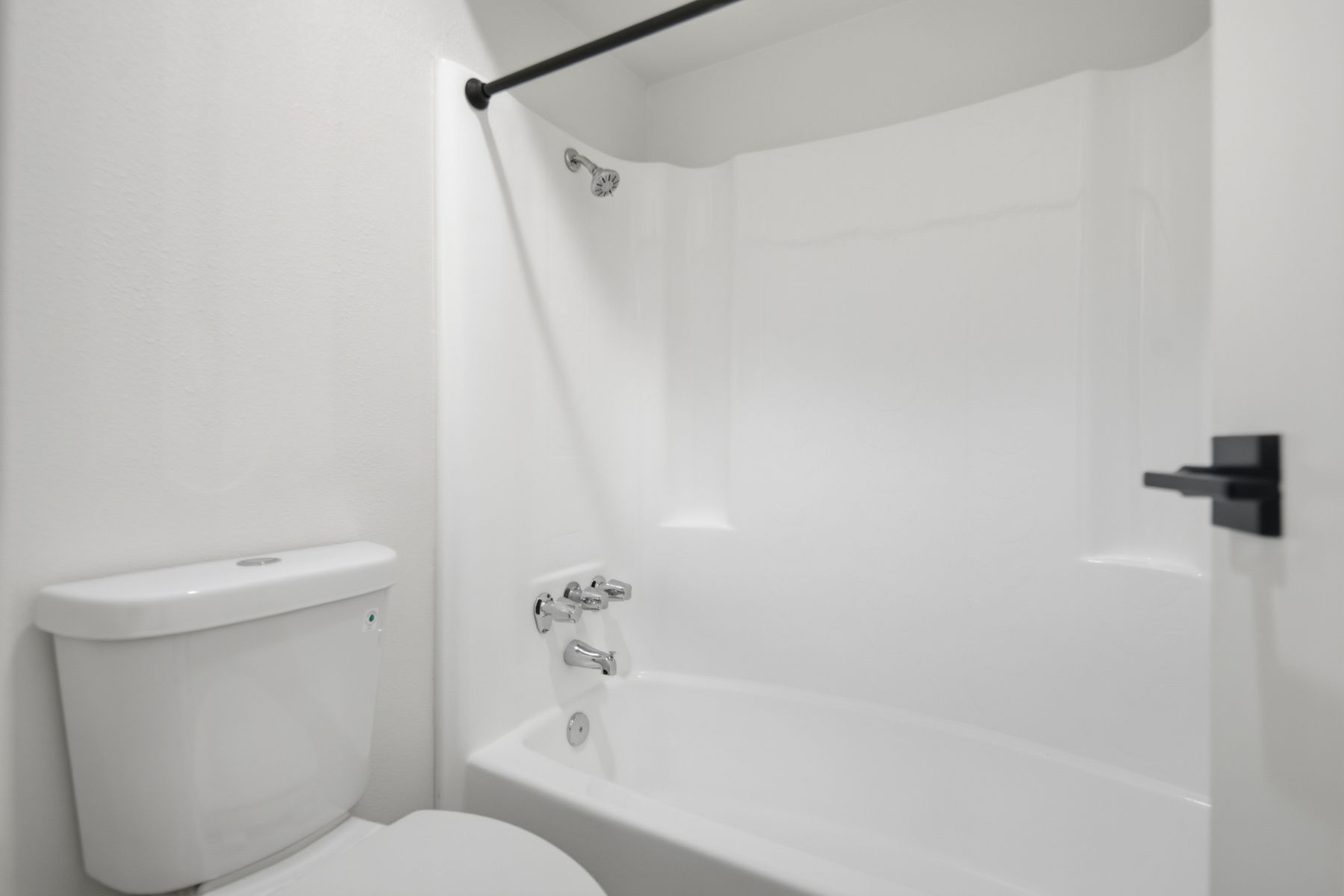 White bathroom with toilet and shower/tub combo. Black shower rod and hardware.
