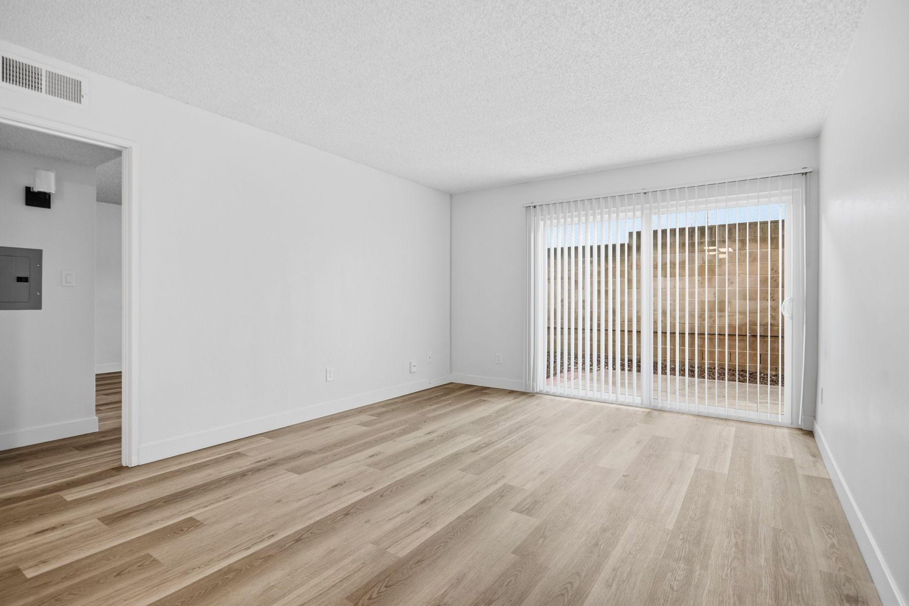 Empty room with light wood floors, white walls, and sliding glass door with blinds.