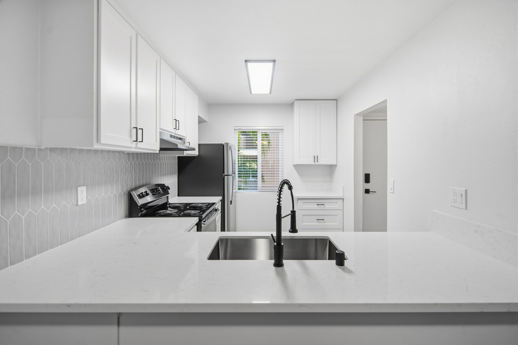 Modern white kitchen with white countertops, backsplash, and cabinets; black appliances and faucet.