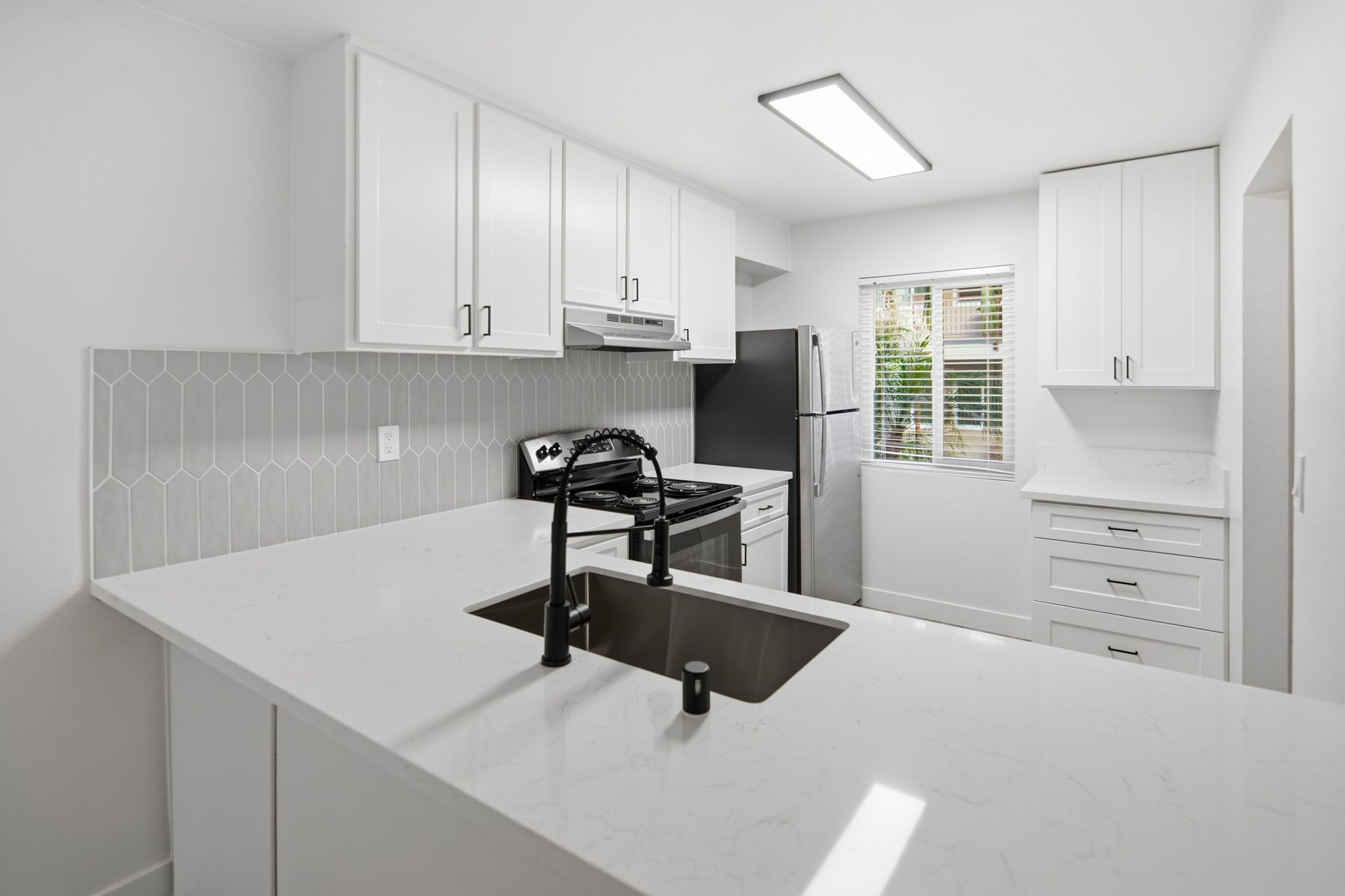 White kitchen with white cabinets, countertops, and gray backsplash. Black faucet and appliances.