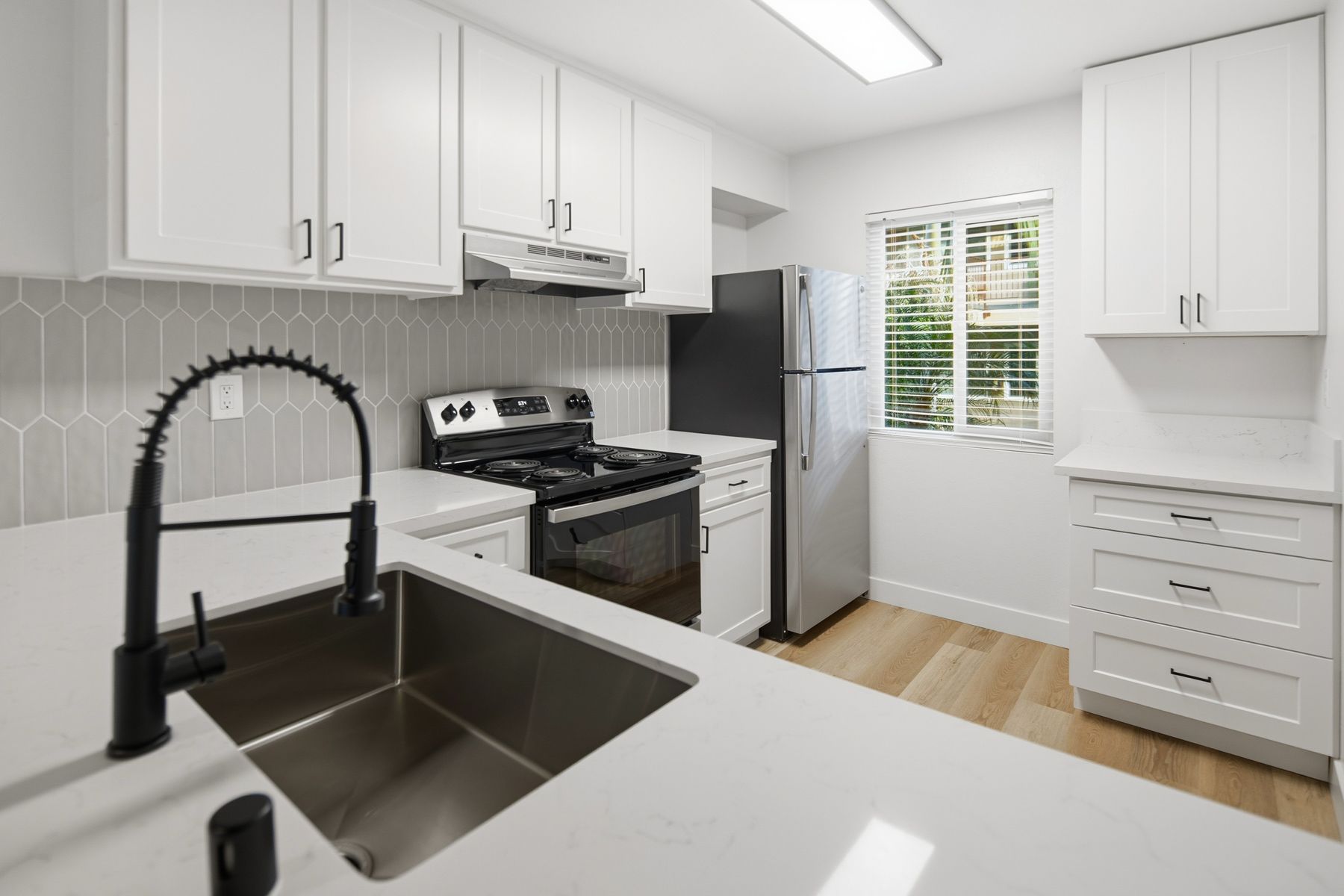 White kitchen with stainless steel appliances, modern black faucet, and a window.