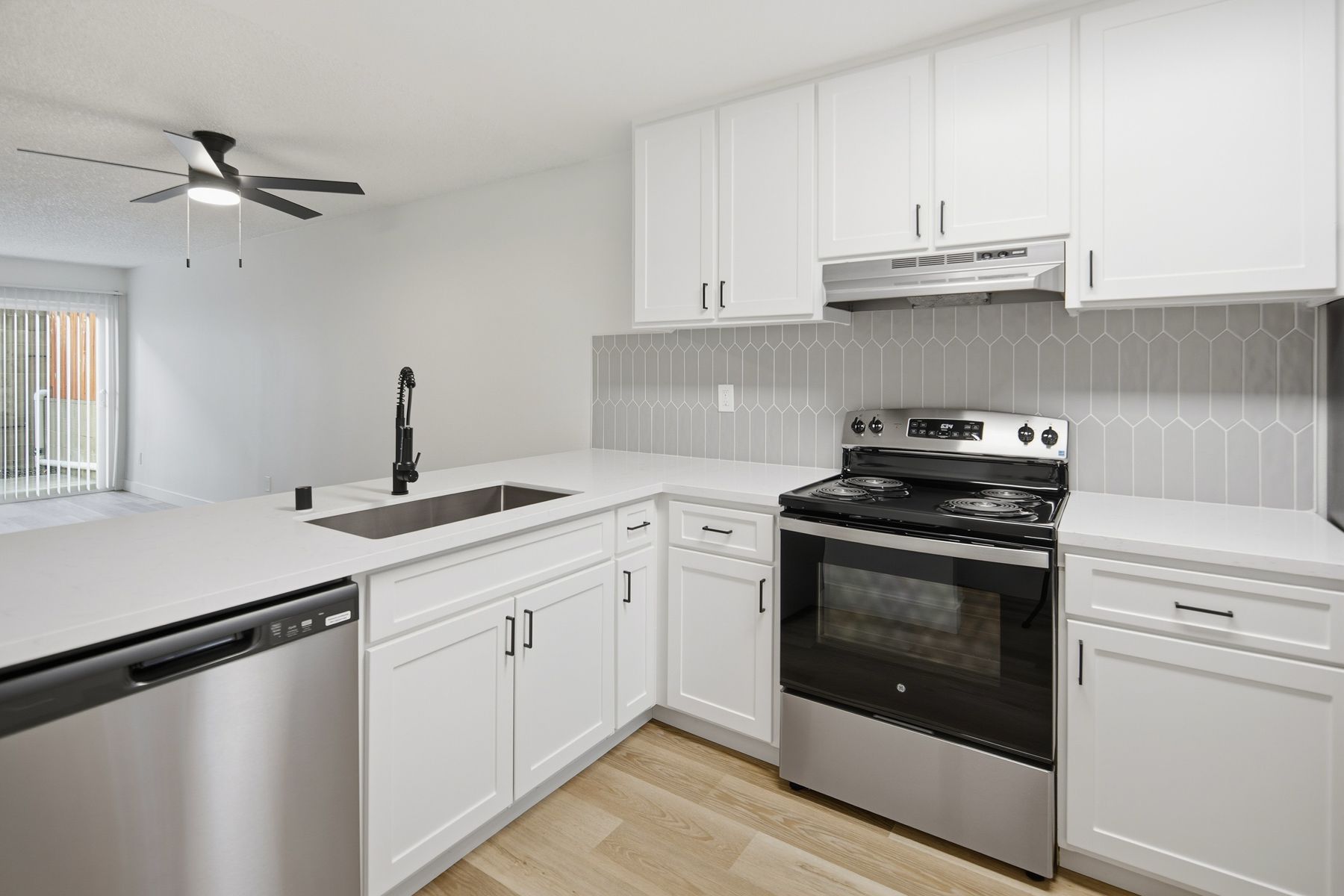 White kitchen with stainless steel appliances, light countertops, and tile backsplash.