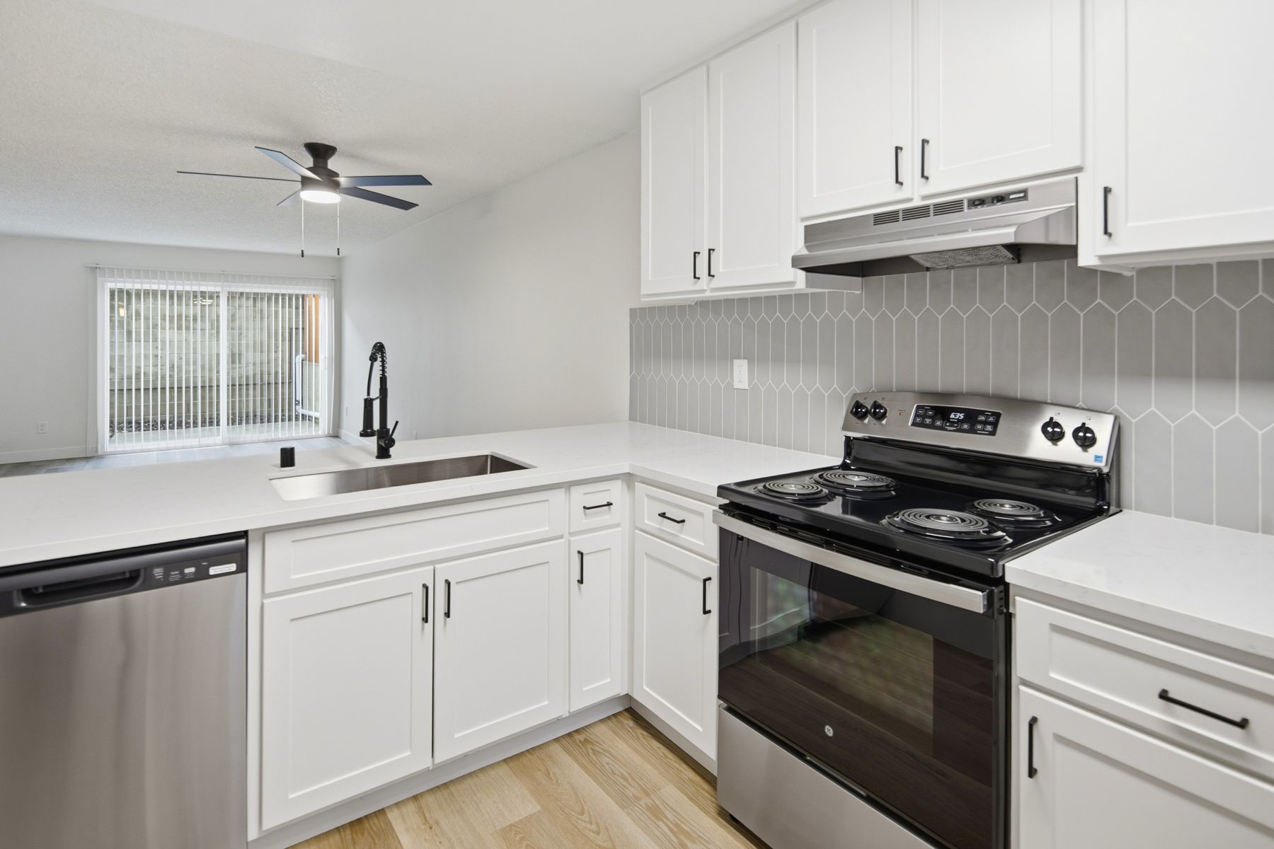 Modern kitchen with white cabinets, stainless steel appliances, and gray backsplash.