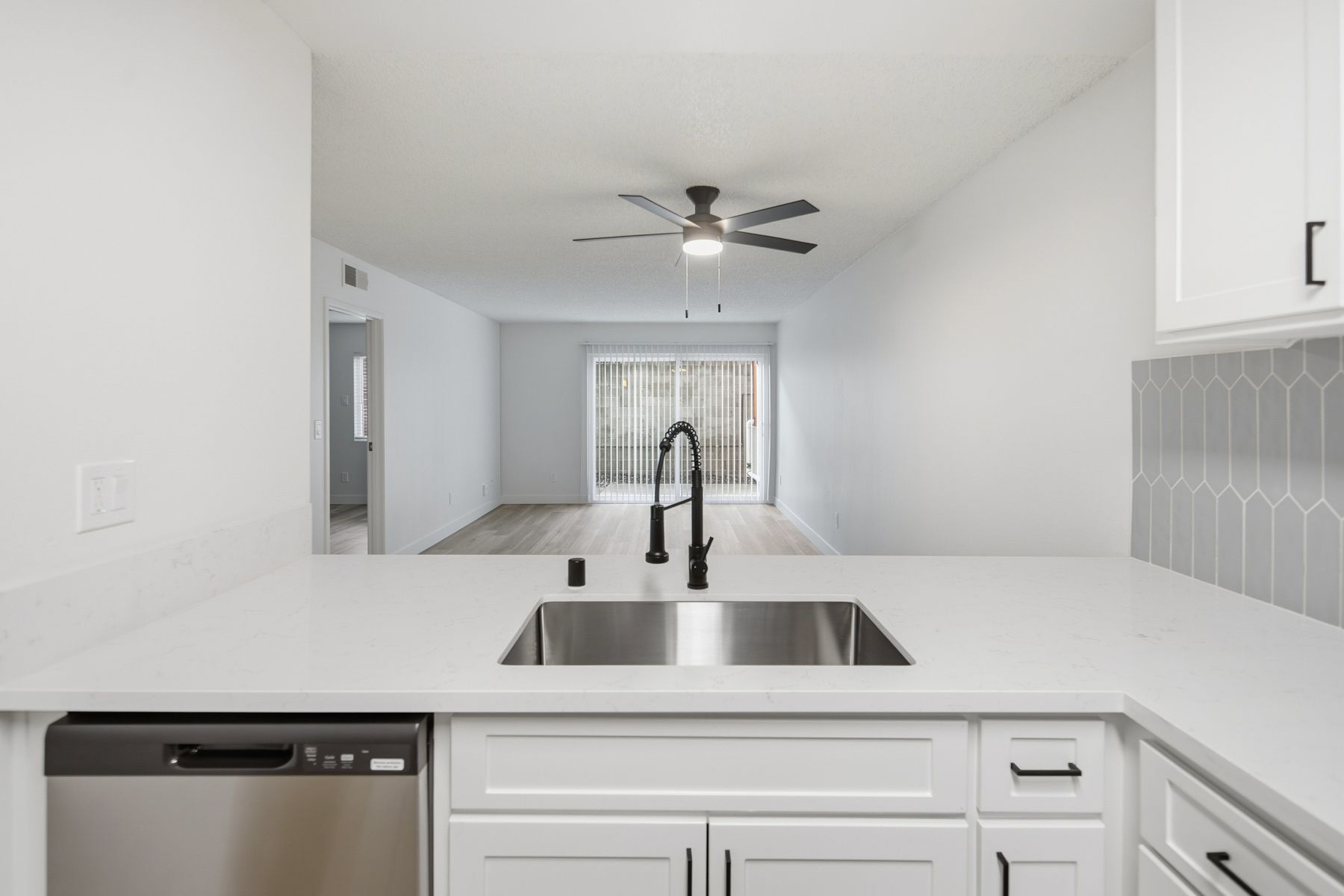 Kitchen with white cabinets and countertop, stainless steel sink and appliances, and view into the living room.