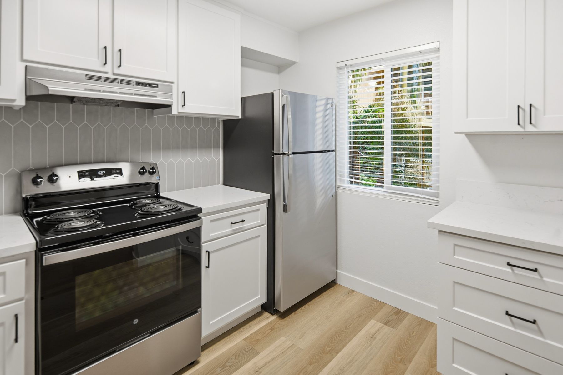 Modern kitchen with white cabinets, stainless steel appliances, and wood flooring.