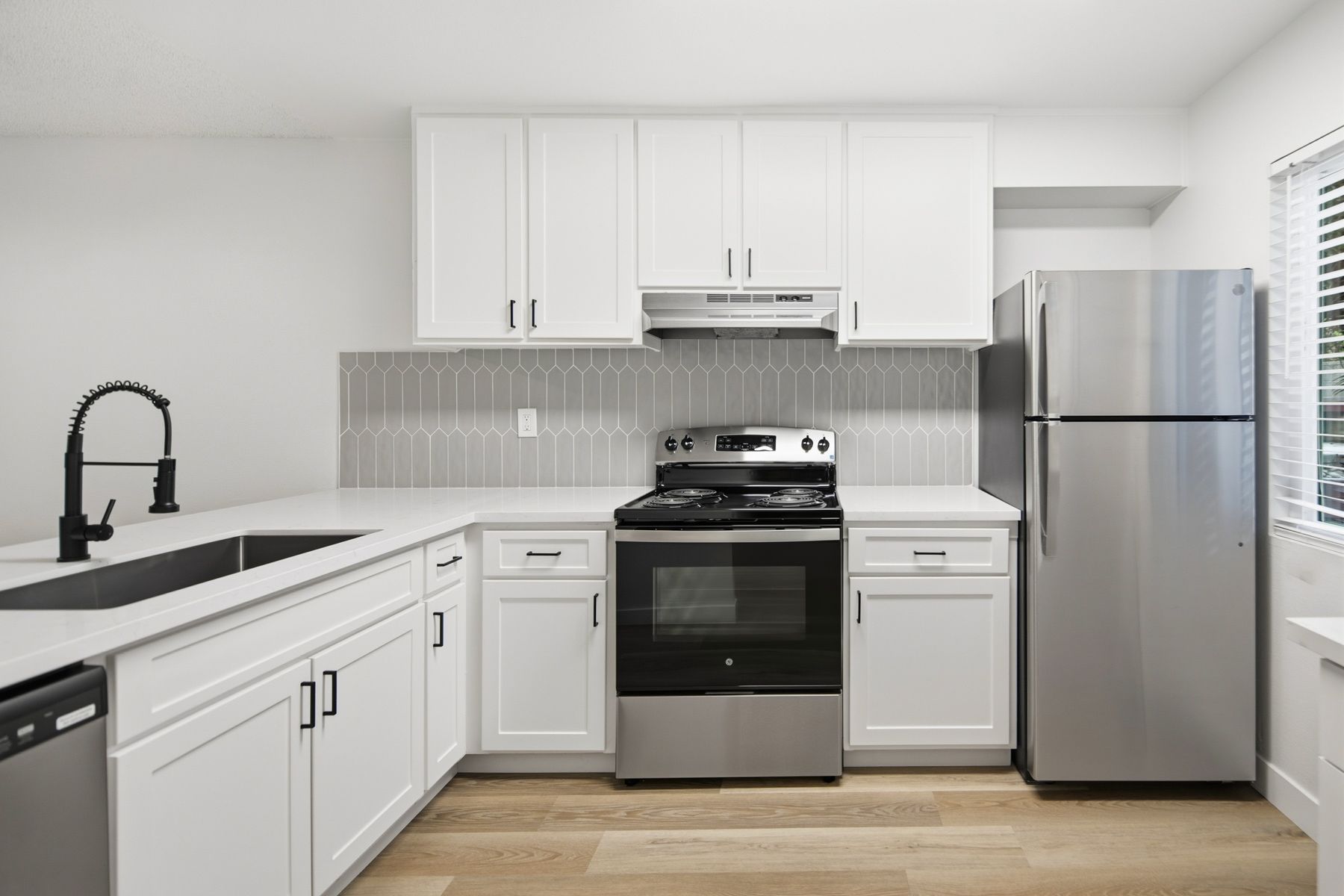 White kitchen with stainless steel appliances and light wood floors.