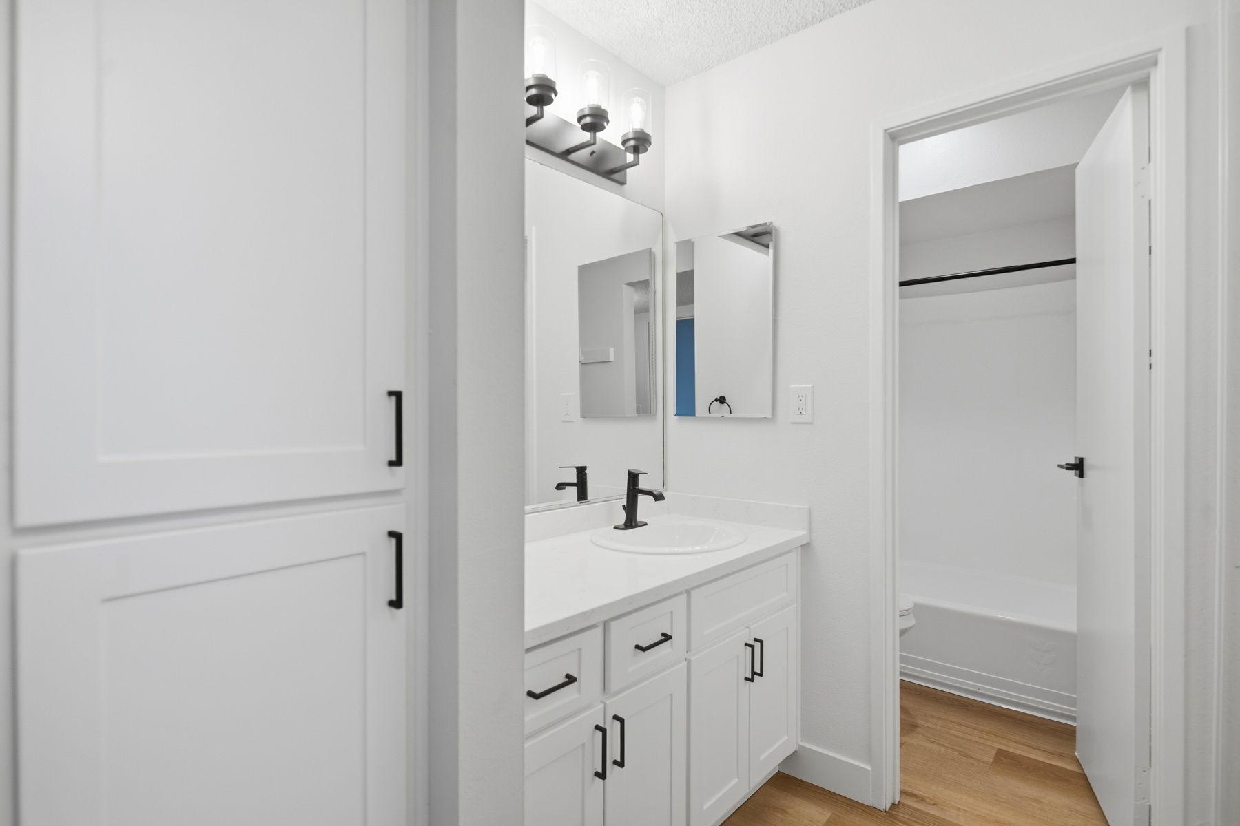 White bathroom with double vanity, black fixtures, and a closet.