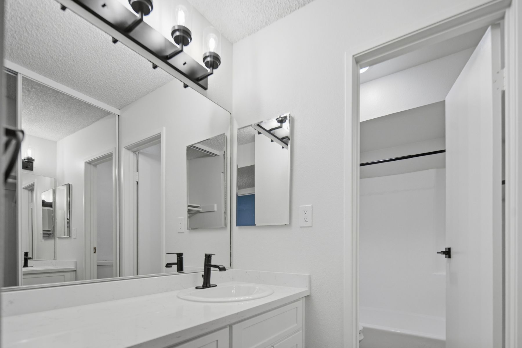 White bathroom with vanity, mirror, and open closet door.