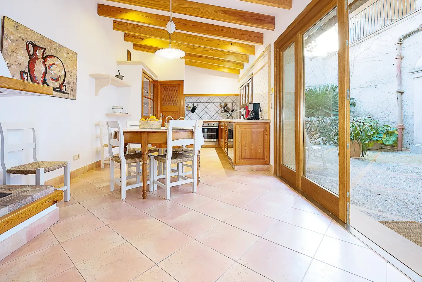 Comedor con mesa, sillas, cocina y puertas de vidrio abiertas a un patio.