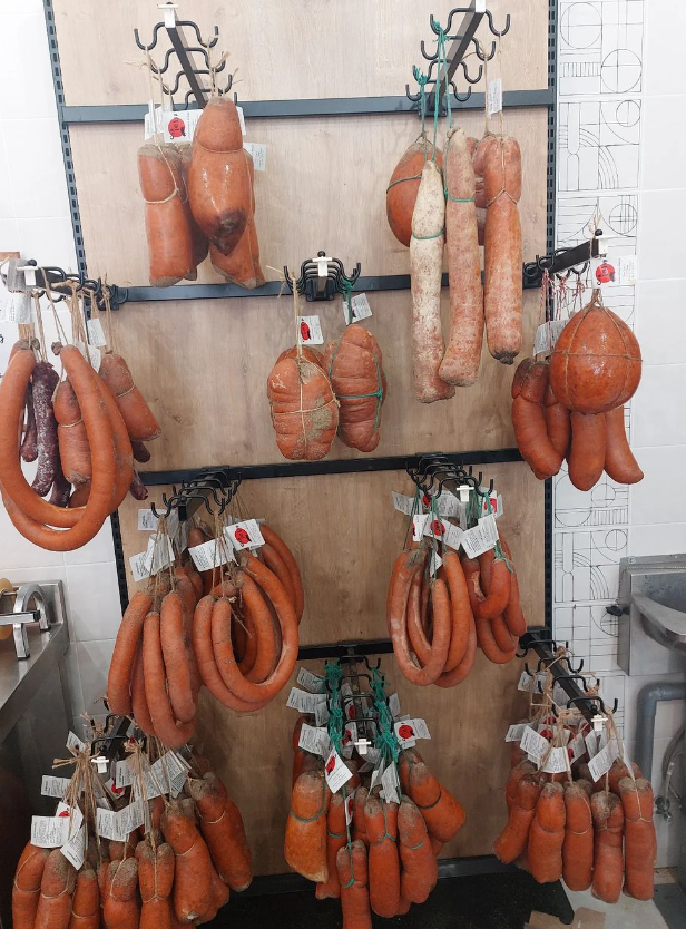 Una exhibición de salchichas de color naranja y embutidos colgados de ganchos en una tabla de madera.