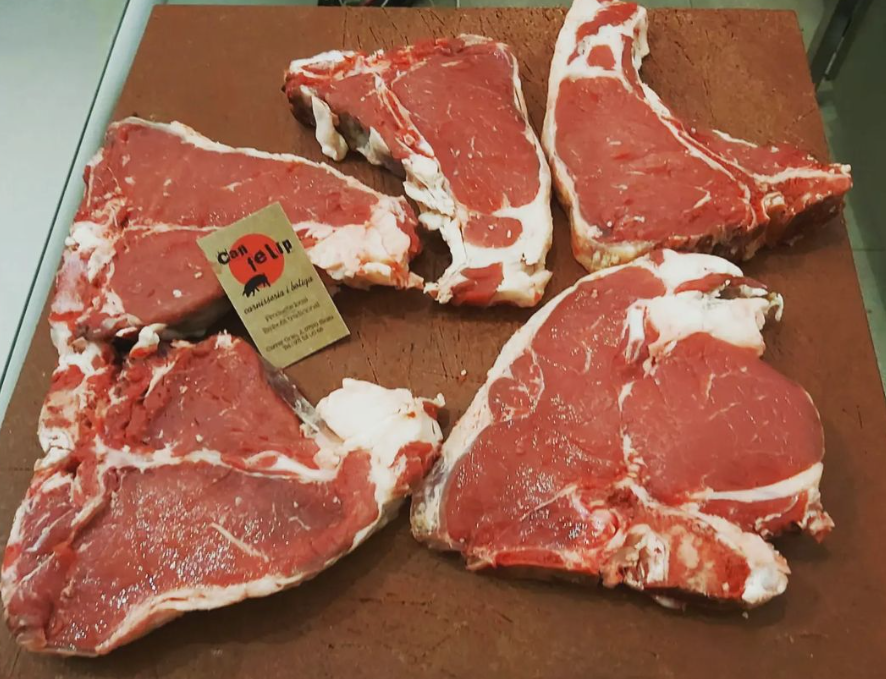 Cinco filetes T-bone crudos en una tabla de carnicero, con un precio pequeño.